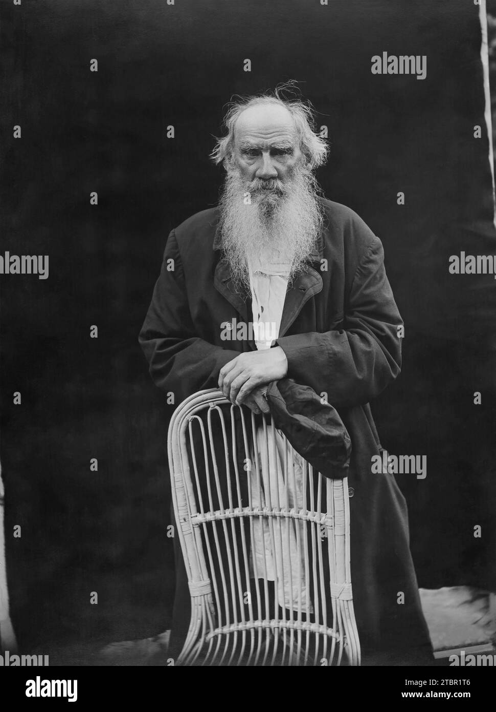 Ritratto di Tolstoj, con un cappotto nero su una blusa bianca. Si mette in piedi, appoggiando le mani piegate sul retro di una sedia di vimini, tenendo un berretto nero in saluto Foto Stock