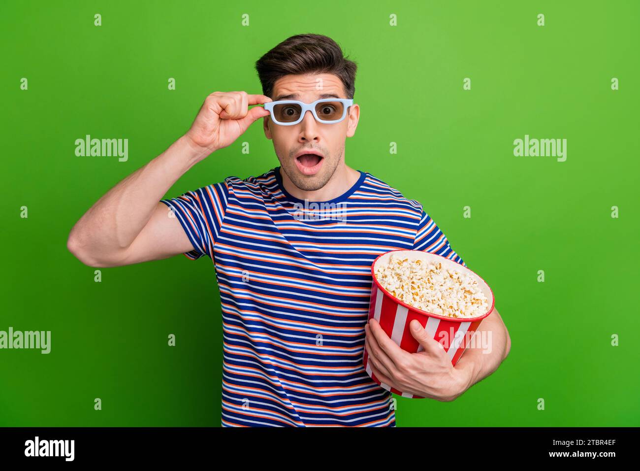 Foto di una t-shirt a righe impressionato che tocca gli occhiali e che fissa incredibili effetti visivi isolati sullo sfondo di colore verde Foto Stock