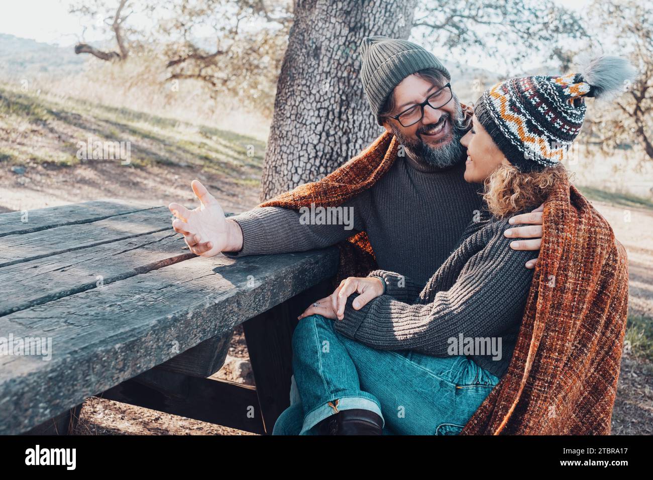 Una coppia di adulti felici si diverte con un'attività di svago all'aperto seduto su una panca di legno e un tavolo al parco durante le vacanze del fine settimana. Un uomo che parla e lo dice a una donna. persone sposate Foto Stock