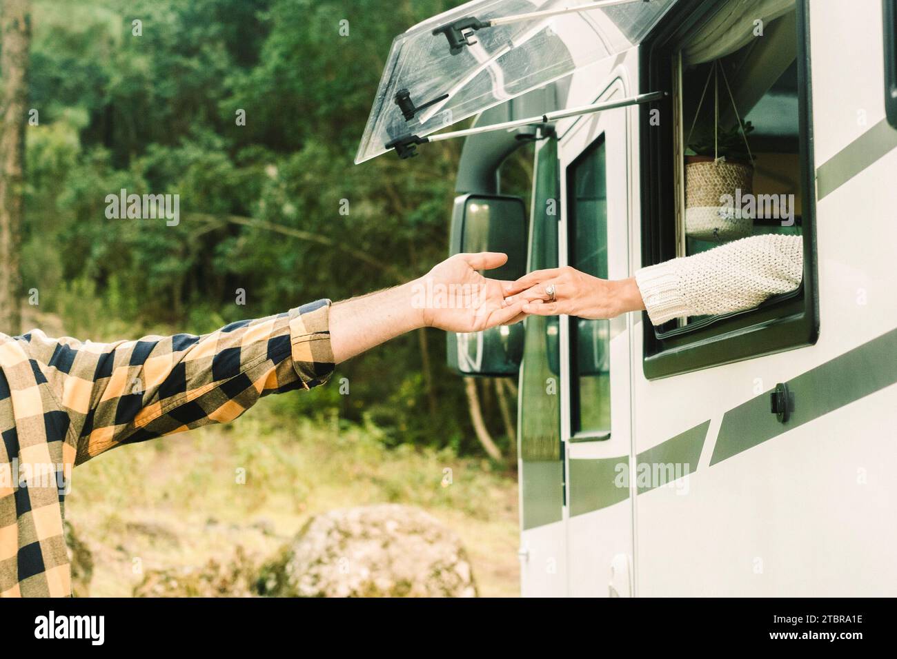 Concetto di persone che viaggiano insieme all'amore. Un uomo e una donna che si toccano le mani l'un l'altro dall'interno di un camper all'esterno. Foresta naturale verde sullo sfondo. Viaggiatore e destinazione. Vanlife Foto Stock