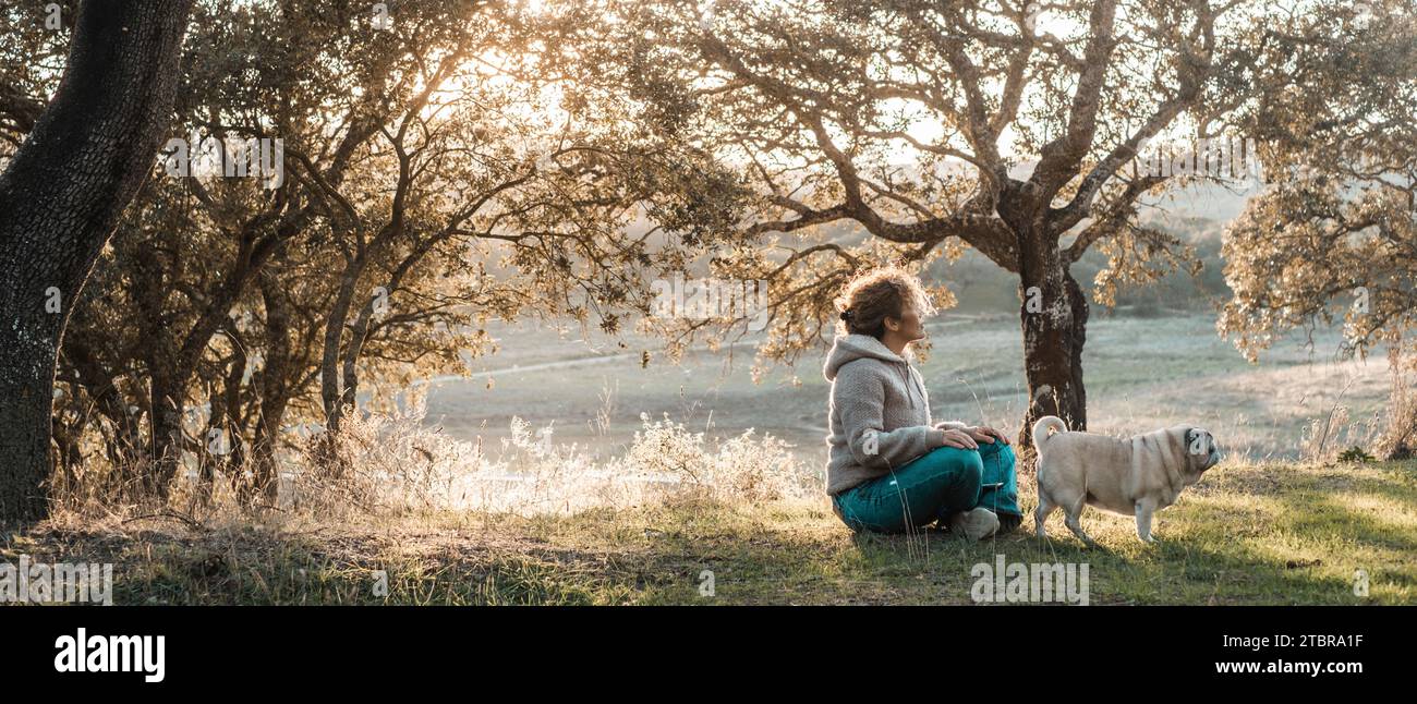 Una donna seduta sull'erba si gode un posto tranquillo e sereno con il suo cane migliore amico. Insieme per sempre persone animali natura. Goditi il tempo libero sul lago. Turismo in campagna. Foto Stock