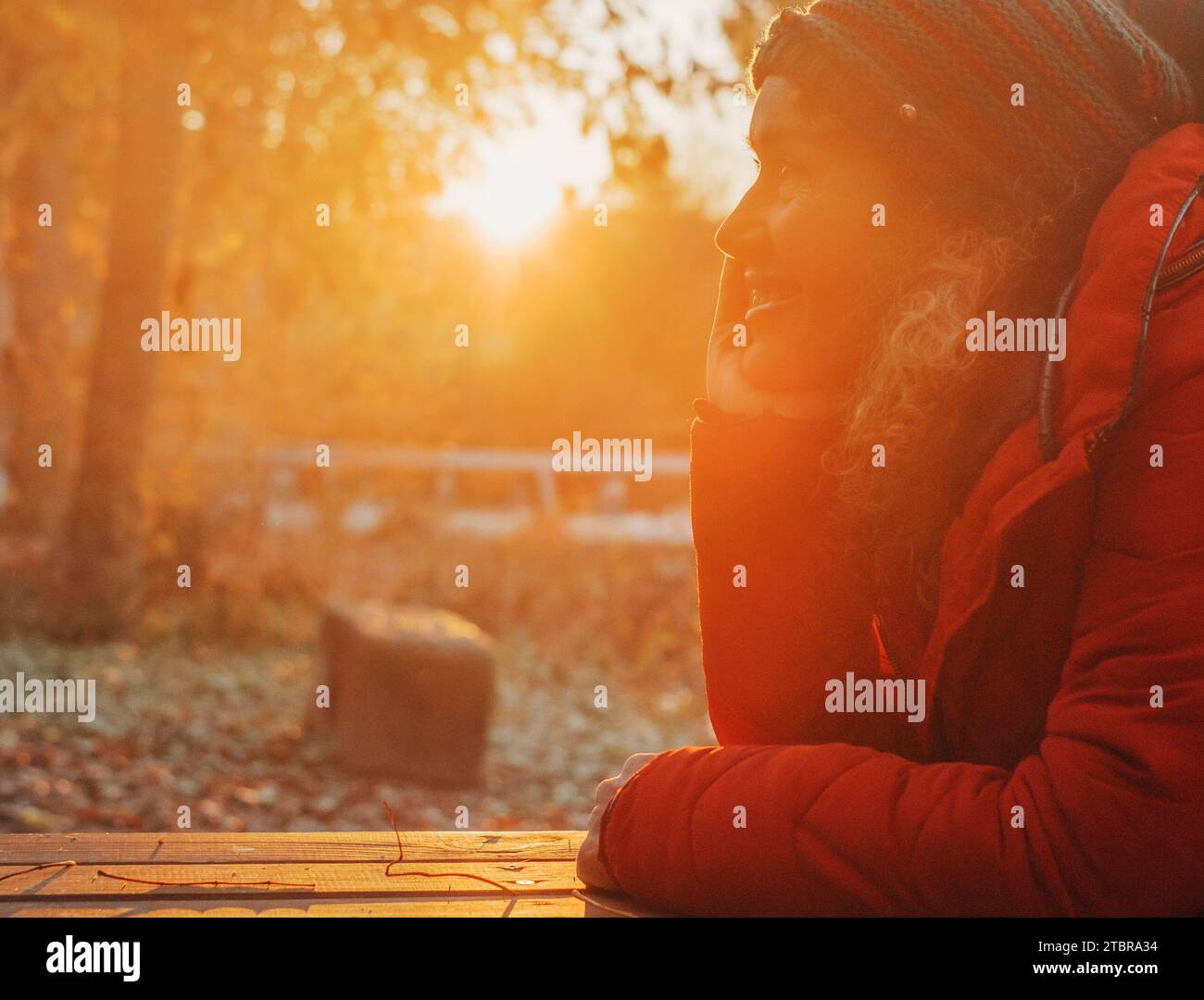 Ritratto laterale di una giovane donna che si rilassa e pensa felice sorridendo. Una donna si diverte con attività all'aperto e con il tramonto autunnale dorato al parco. La natura sullo sfondo. Benessere sereno Foto Stock