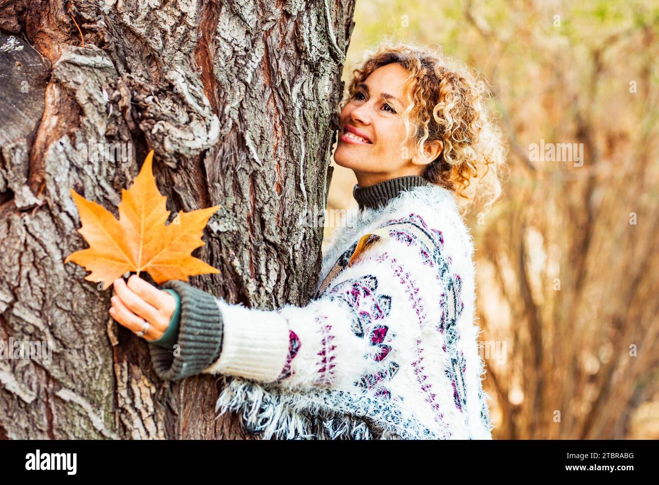 Una donna adulta felice abbraccia un albero e sorride in autunno, attività ricreative all'aperto. Stile di vita naturale e persone che amano la natura. Legni e alberi di colore giallo sullo sfondo. Donne che si divertono al parco Foto Stock