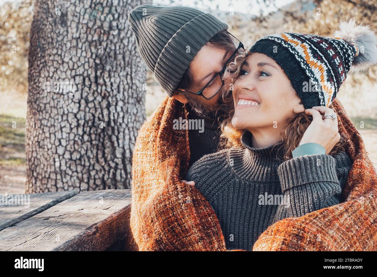 Coppia felice in una romantica attività di svago insieme coccolandosi al parco. L'autunno ama le persone. Uomo che abbraccia e lega una donna carina seduta su una panchina di legno con foglie gialle e alberi sullo sfondo Foto Stock