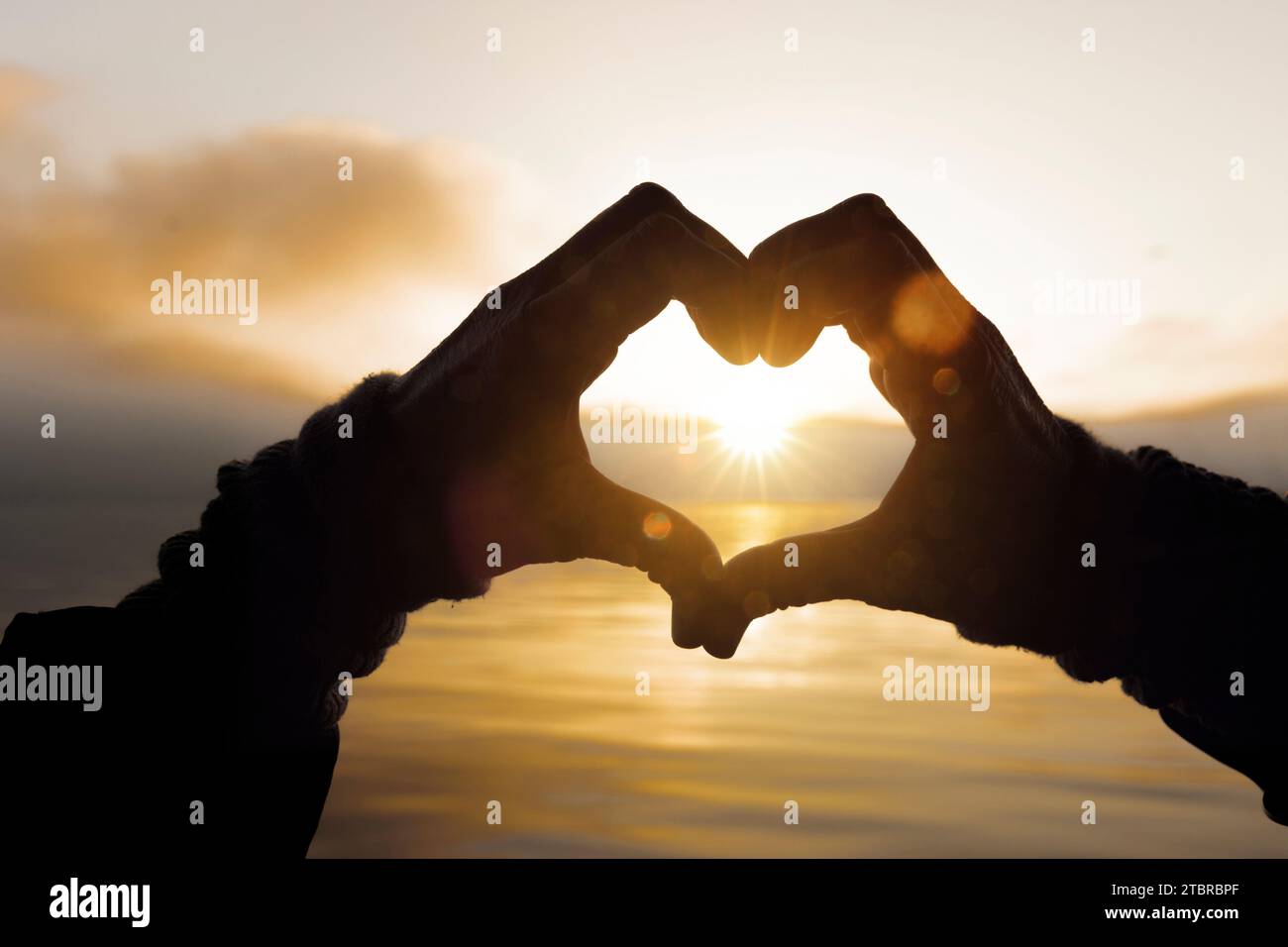 Due mani formano un cuore di fronte a un lago al tramonto Foto Stock