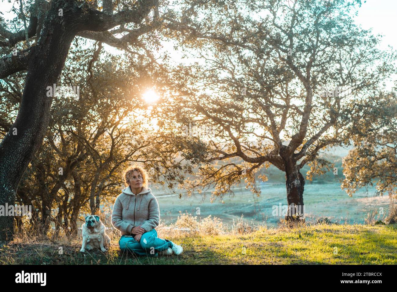 Coppia felice, donna e cane, divertiti con attività ricreative all'aperto seduti a terra in un paesaggio paesaggistico autunnale con il fiume sullo sfondo e la luce del sole al tramonto. Gente felice amicizia animale Foto Stock