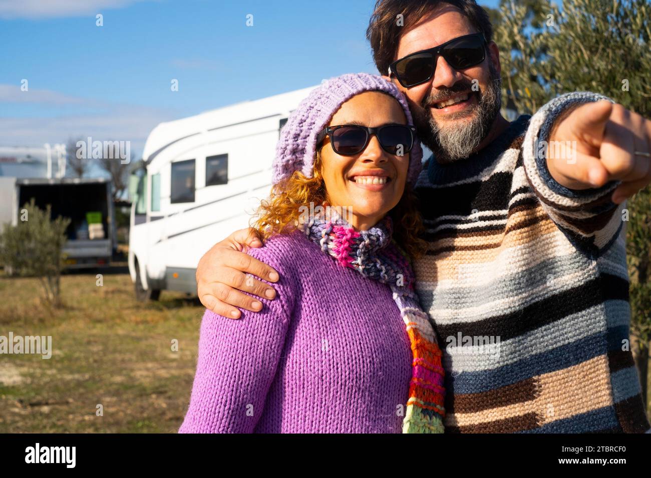 Una felice coppia di turisti, uomini e donne, che puntano e ammirano la destinazione insieme al sorriso e al camper camper in camper sullo sfondo. Vacanza con veicolo a noleggio. Vacanze estive Foto Stock