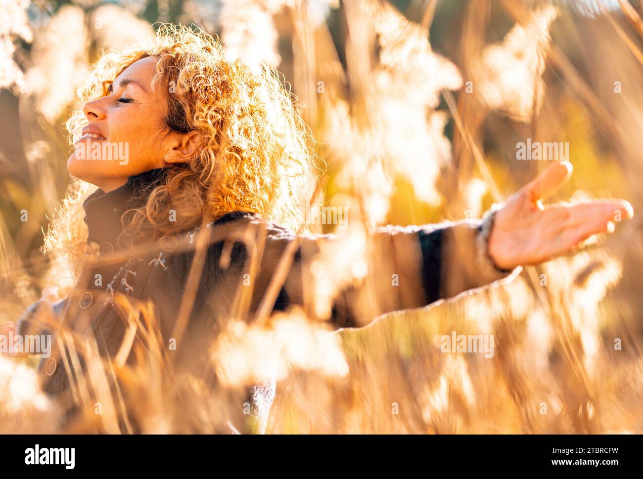 Una donna felice che si allunga alle braccia e si goda la natura sorridendo in un campo dorato con la luce del sole al tramonto. Persone e attività ricreative all'aperto. Felicità e benessere donna stile di vita. Libertà. Overjoy Life Foto Stock