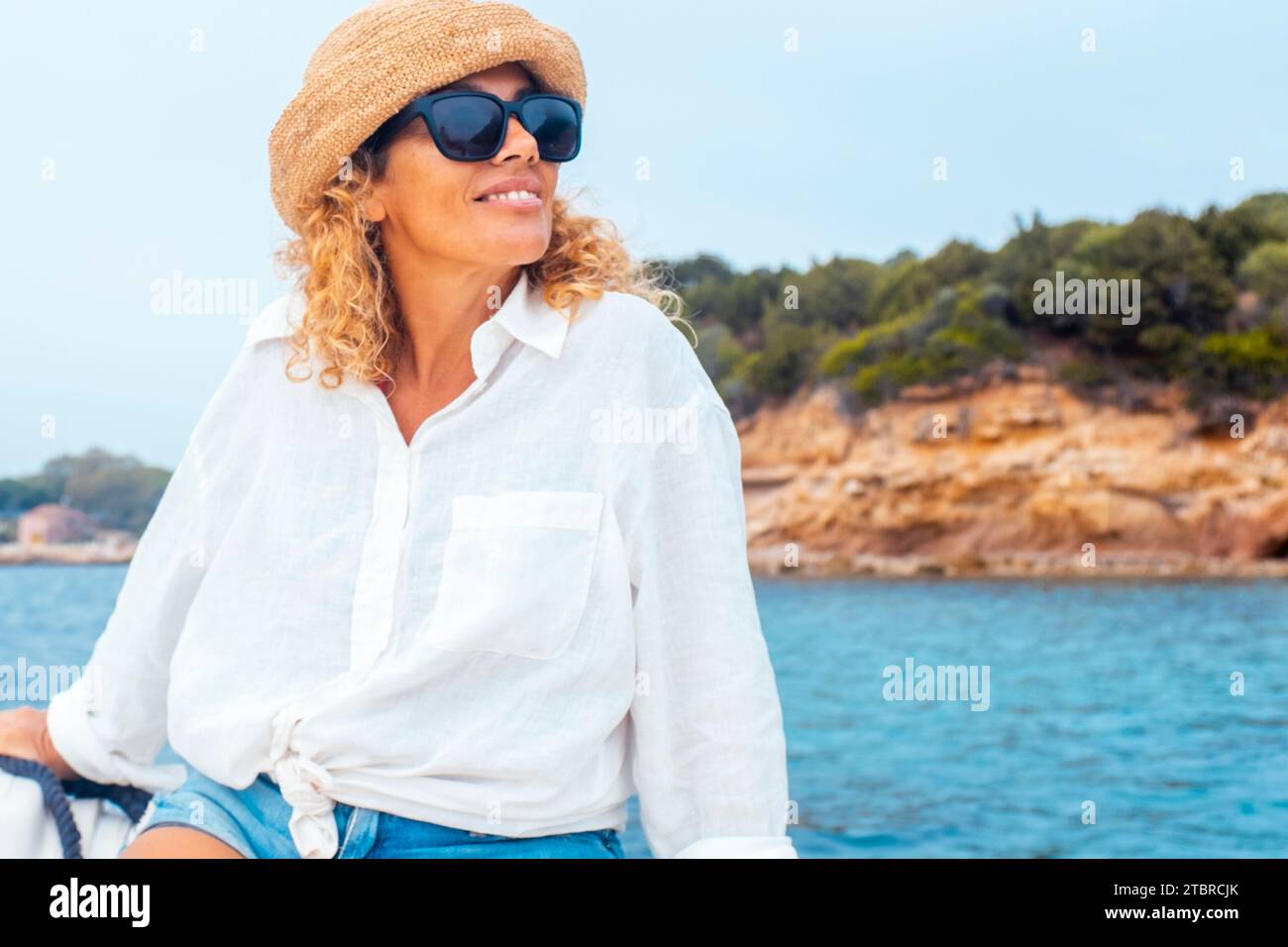 Una giovane e serena seduta su una barca per un'escursione lungo la costa durante le vacanze estive. Isola sullo sfondo. Concetto di viaggio e libertà di vita persone al mare Foto Stock