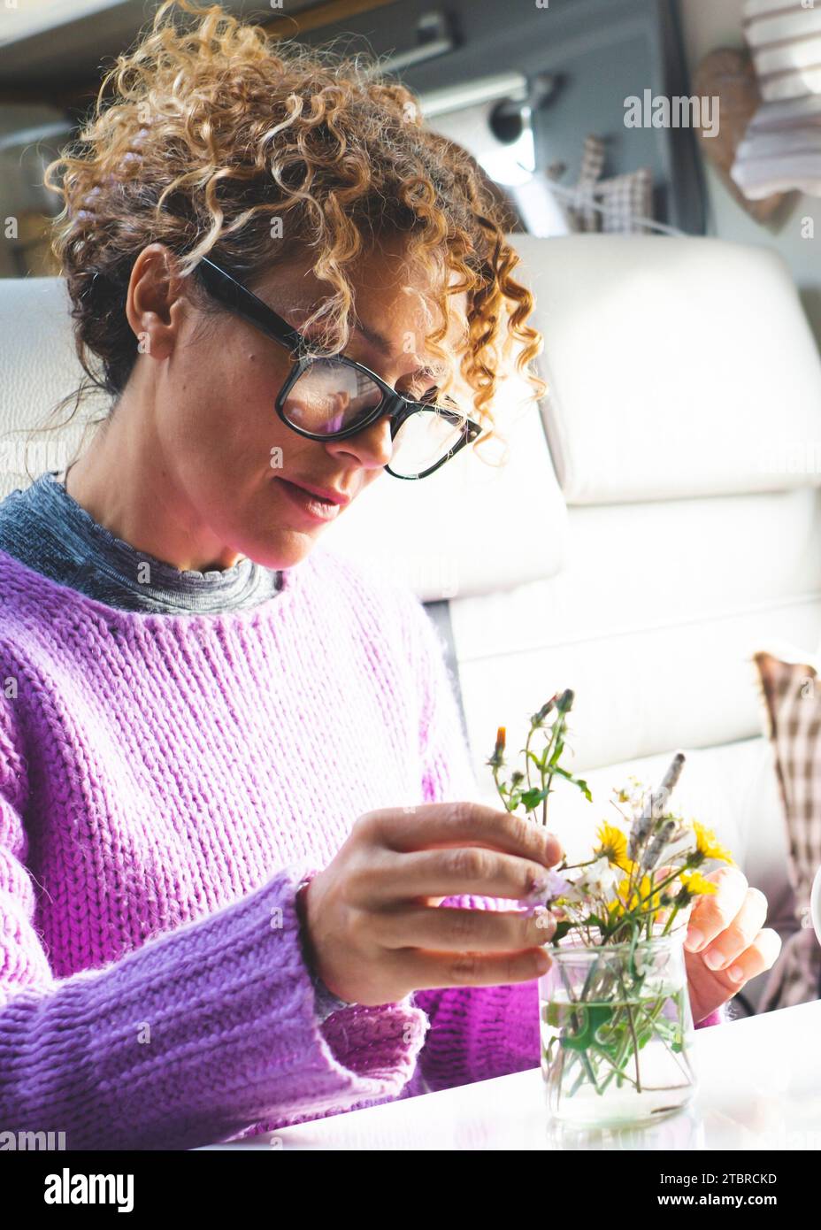 Una donna adulta che si prende cura di piante e fiori all'interno di un camper, un piccolo camper moderno da solo. Persone che vivono vanlife a tempo pieno. Persone e natura. Divertimento al coperto per giovani e mature Foto Stock