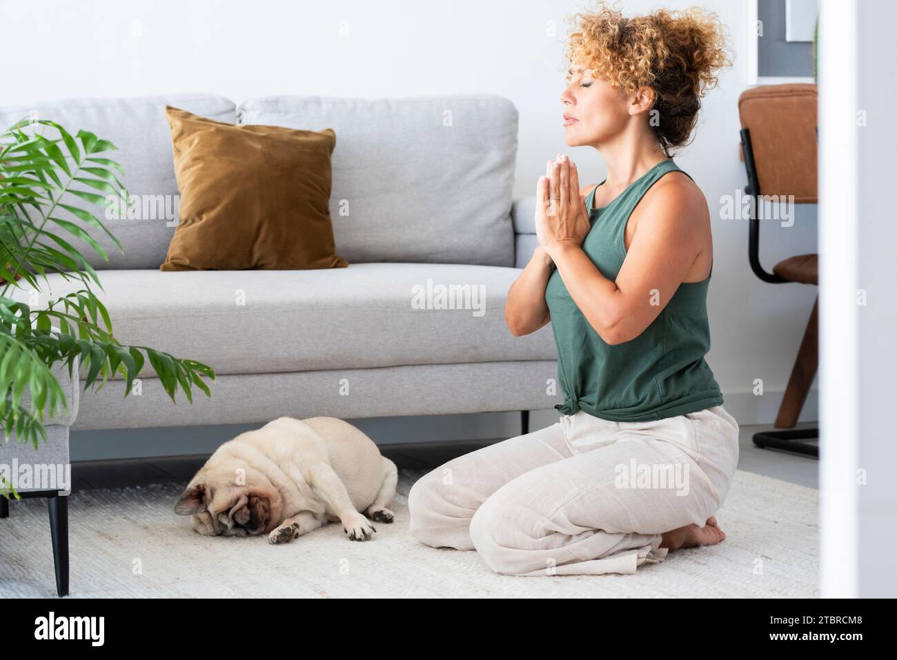 Una giovane donna adulta che fa esercizi di yoga a casa da sola in salotto. Allenamento sano pilates stile di vita persone in attività sportive indoor. Benessere ed equilibrio mentale interiore donna matura consapevole Foto Stock