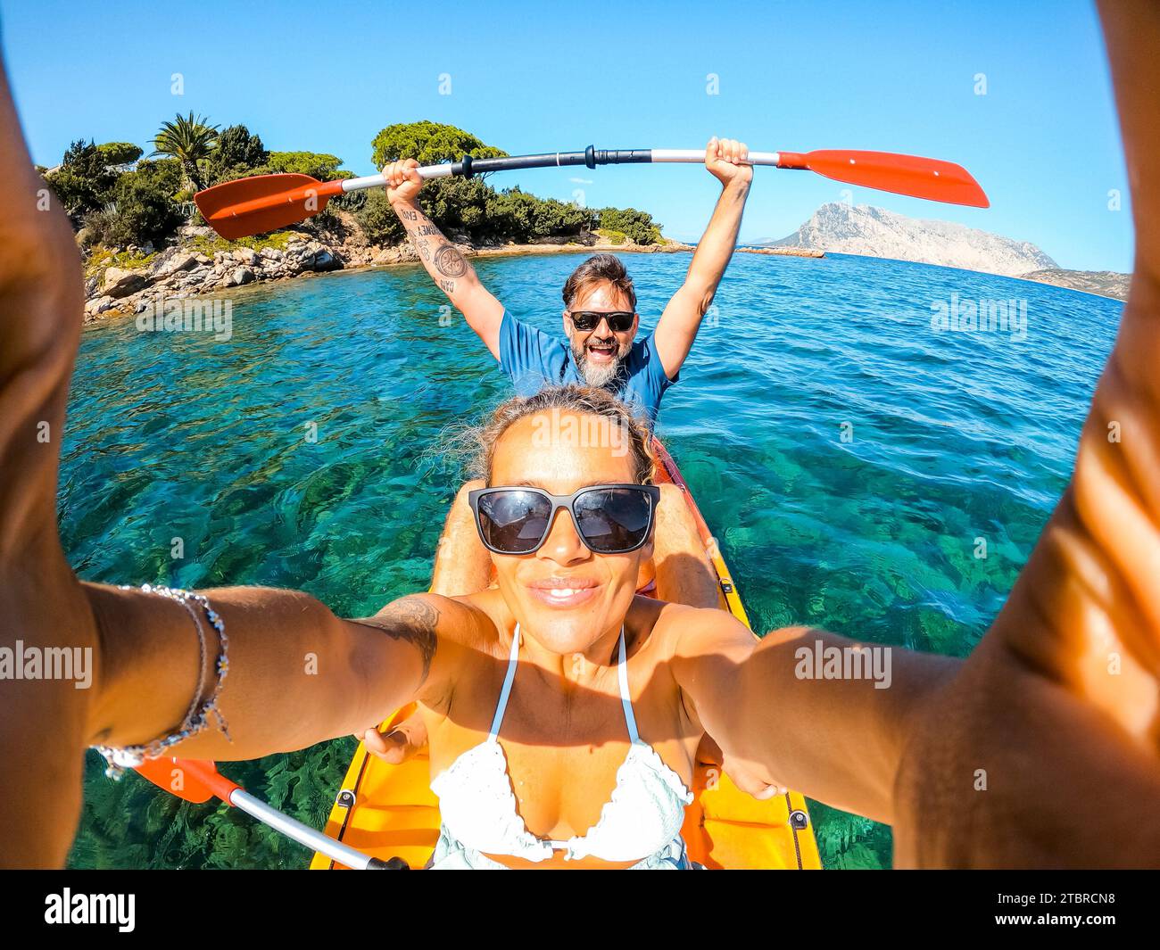 Felicissima coppia di turisti adulti e donne caucasici che scattano selfie all'interno di una canoa in kayak con acqua blu pulita dell'oceano e costa sullo sfondo. Viaggi e vacanze estive Foto Stock