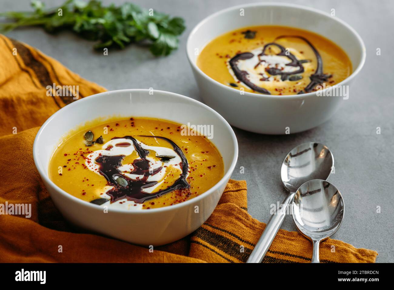 Ciotole con zuppa di zucca fatta in casa con panna, olio di zucca e semi come condimento e coriandolo Foto Stock