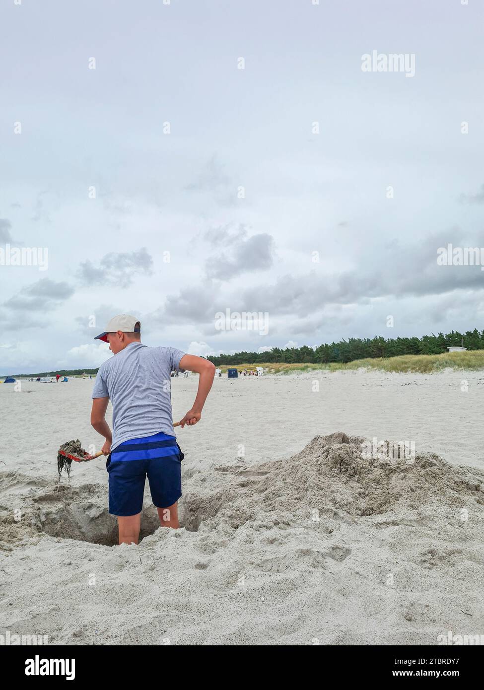 Germania, Meclemburgo-Pomerania occidentale, penisola Fischland-Darß-Zingst, Prerow, un adolescente si trova in un buco di sabbia sulla spiaggia con una pala di alghe in mano Foto Stock