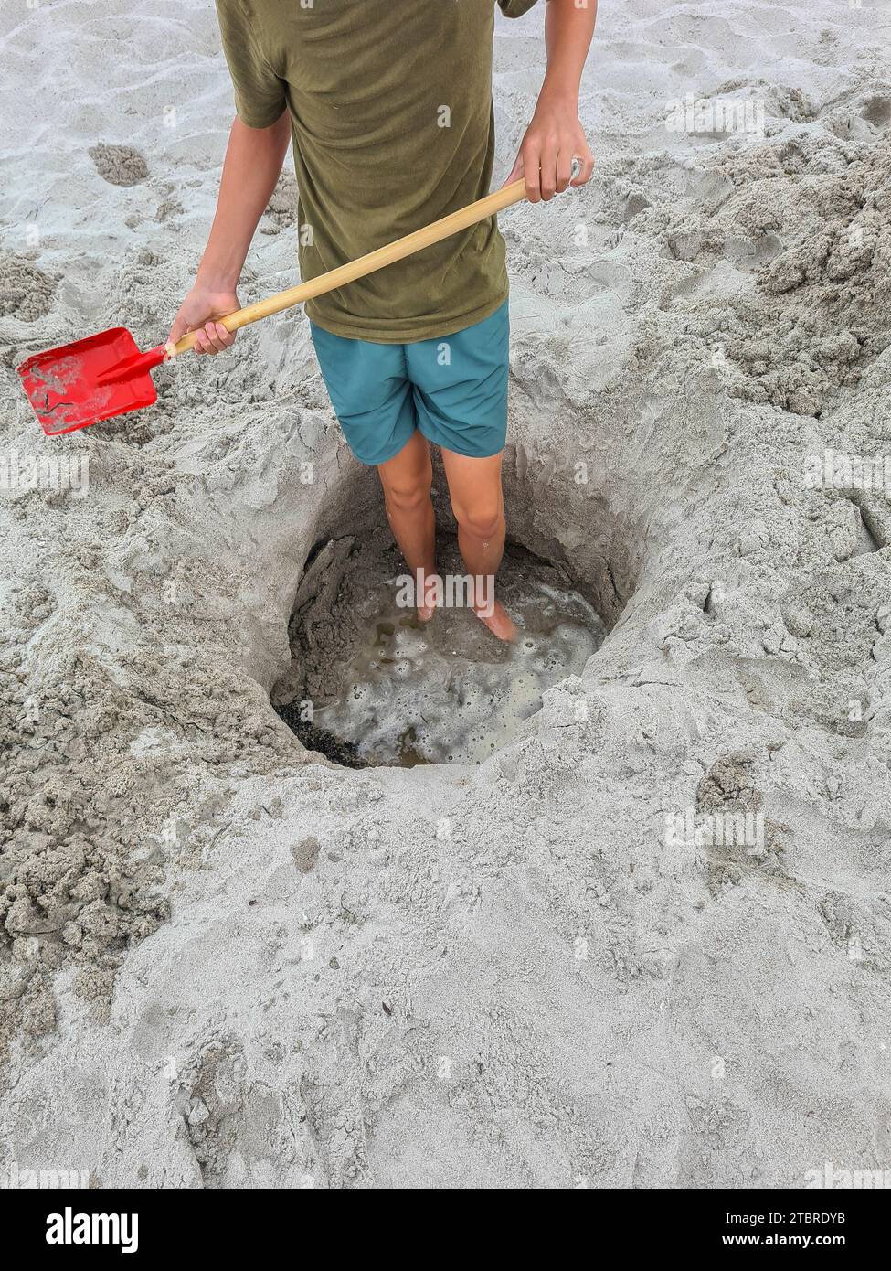 Germania, Meclemburgo-Pomerania occidentale, penisola Fischland-Darß-Zingst, Prerow, un adolescente si trova in un buco di sabbia sulla spiaggia con una pala in mano Foto Stock