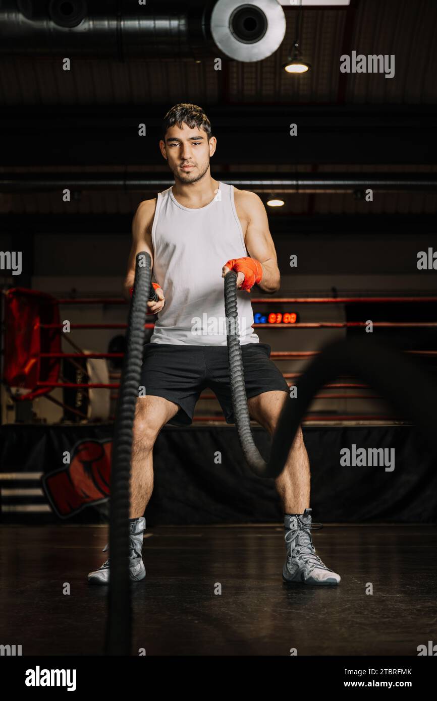 Verticale foto uomo giovane adulto corsa mista, con bende rosse sulle mani e abbigliamento sportivo, allenamento con le corde in una palestra di boxe. Sport e REC Foto Stock