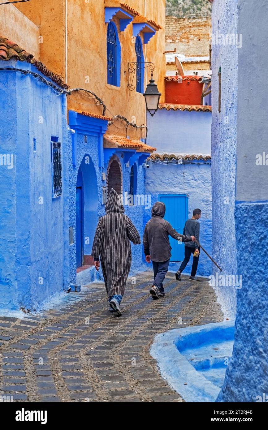Uomo musulmano che indossa la tradizionale djellaba / jillaba islamica camminando attraverso uno stretto vicolo blu nella medina della città di Chefchaouen / Chaouen, Marocco Foto Stock