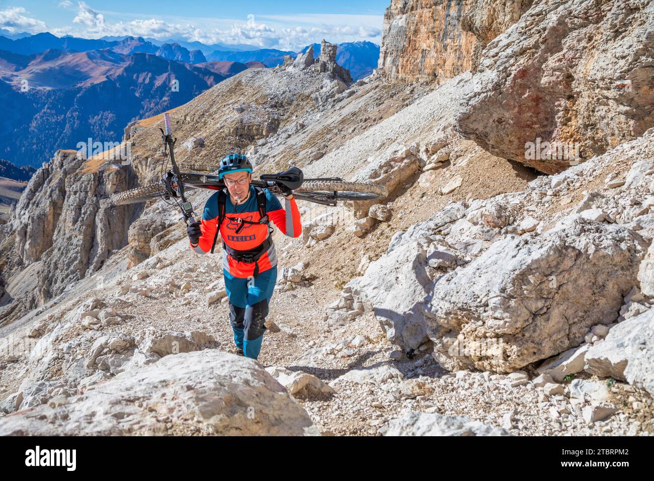 Italia, Dolomiti, ciclista alpinista su un sentiero alpino che porta la mountain bike sulle spalle in un tratto molto difficile Foto Stock
