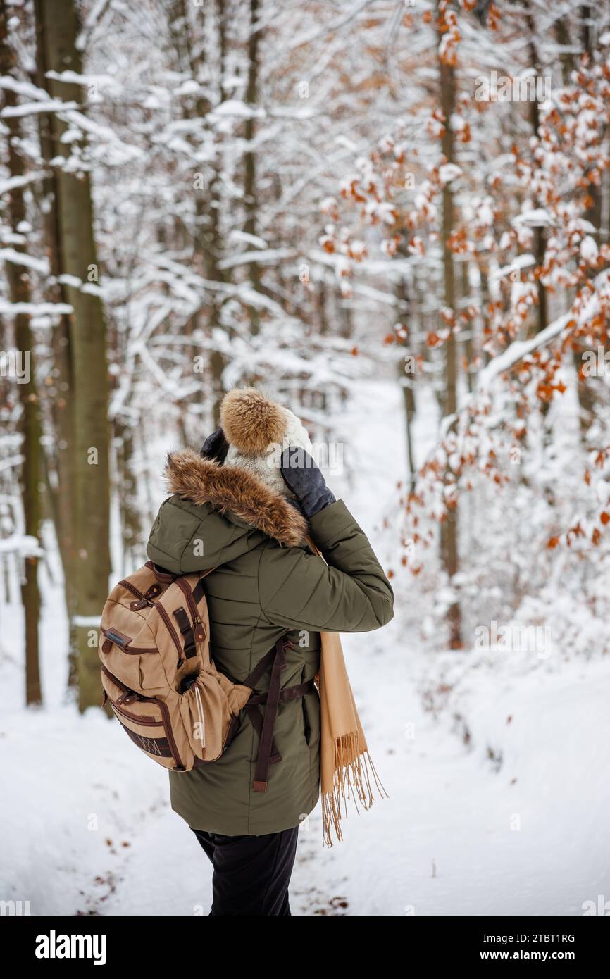 La donna che indossa cappotto, cappello in maglia e guanti da guanti sta facendo escursioni sulla neve nella foresta invernale. Attività all'aperto con clima freddo Foto Stock