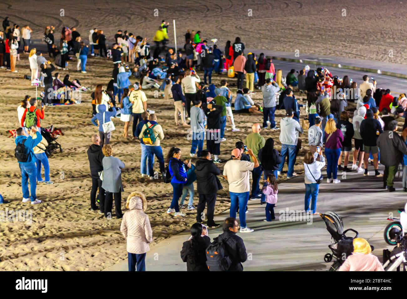 Una folla di persone in piedi sulla spiaggia di notte guardando il cielo guardando uno spettacolo di droni Foto Stock