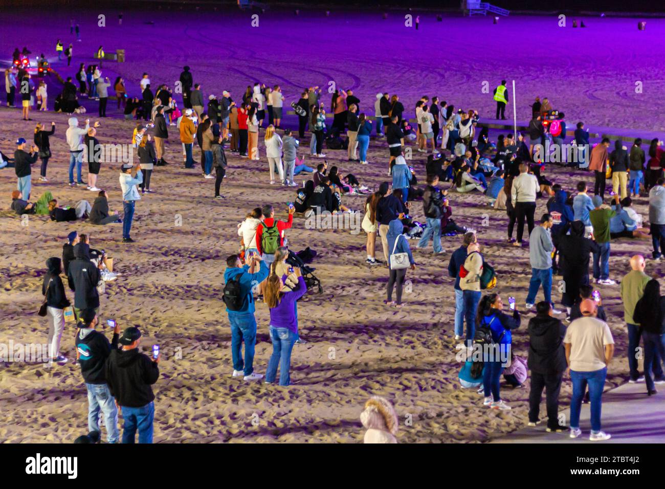 Una folla di persone in piedi sulla spiaggia di notte guardando il cielo guardando uno spettacolo di droni Foto Stock