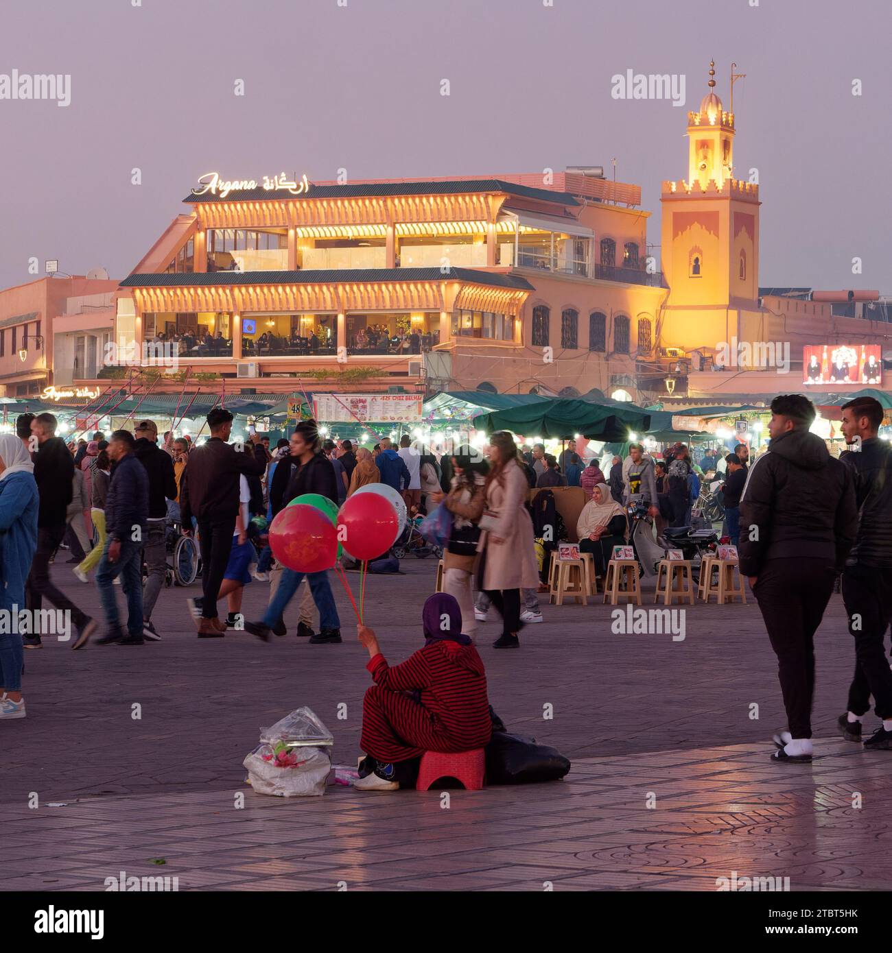 Lady vende palloncini al mercato di Jemaa el-Fnaa di notte con un ristorante dorato alle spalle a Marrakech, alias Marrakech, Marocco, 8 dicembre 2023 Foto Stock