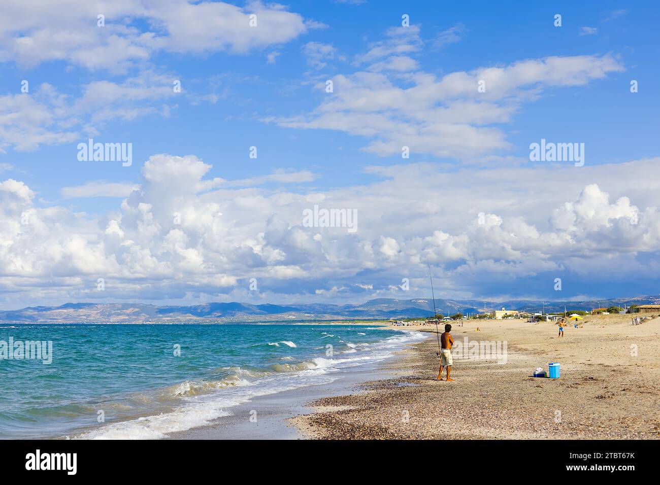 Sulla spiaggia di Plata Mona, Sardegna, Italia, un pescatore sardo è raffigurato con una canna. L'immagine mostra la spiaggia e le montagne lontane. Foto Stock