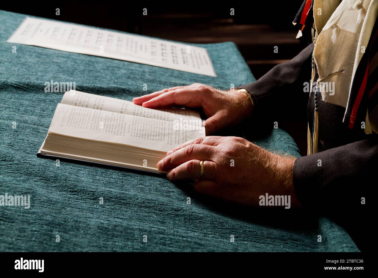Mani anziane che leggono un libro cerimoniale con sfondo musicale Foto Stock