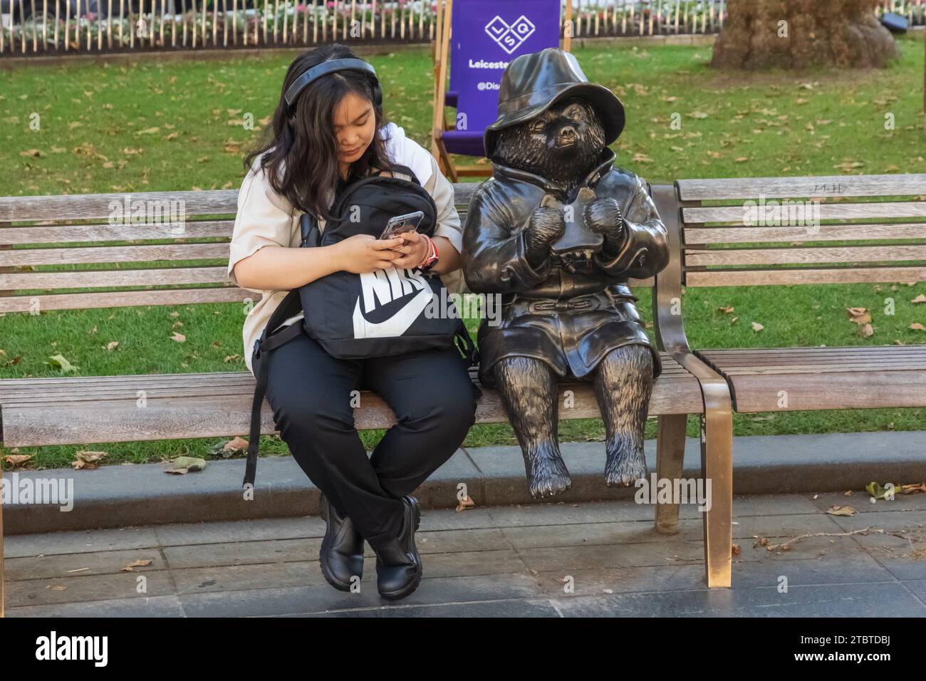 Inghilterra, Londra, Leicester Square, donna turistica asiatica seduta accanto alla Statua dell'Orso Paddington Foto Stock