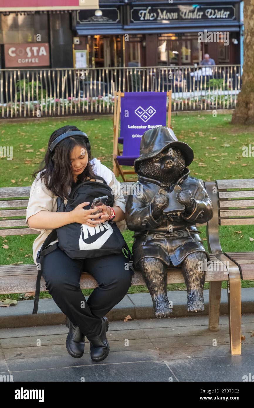 Inghilterra, Londra, Leicester Square, donna turistica asiatica seduta accanto alla Statua dell'Orso Paddington Foto Stock