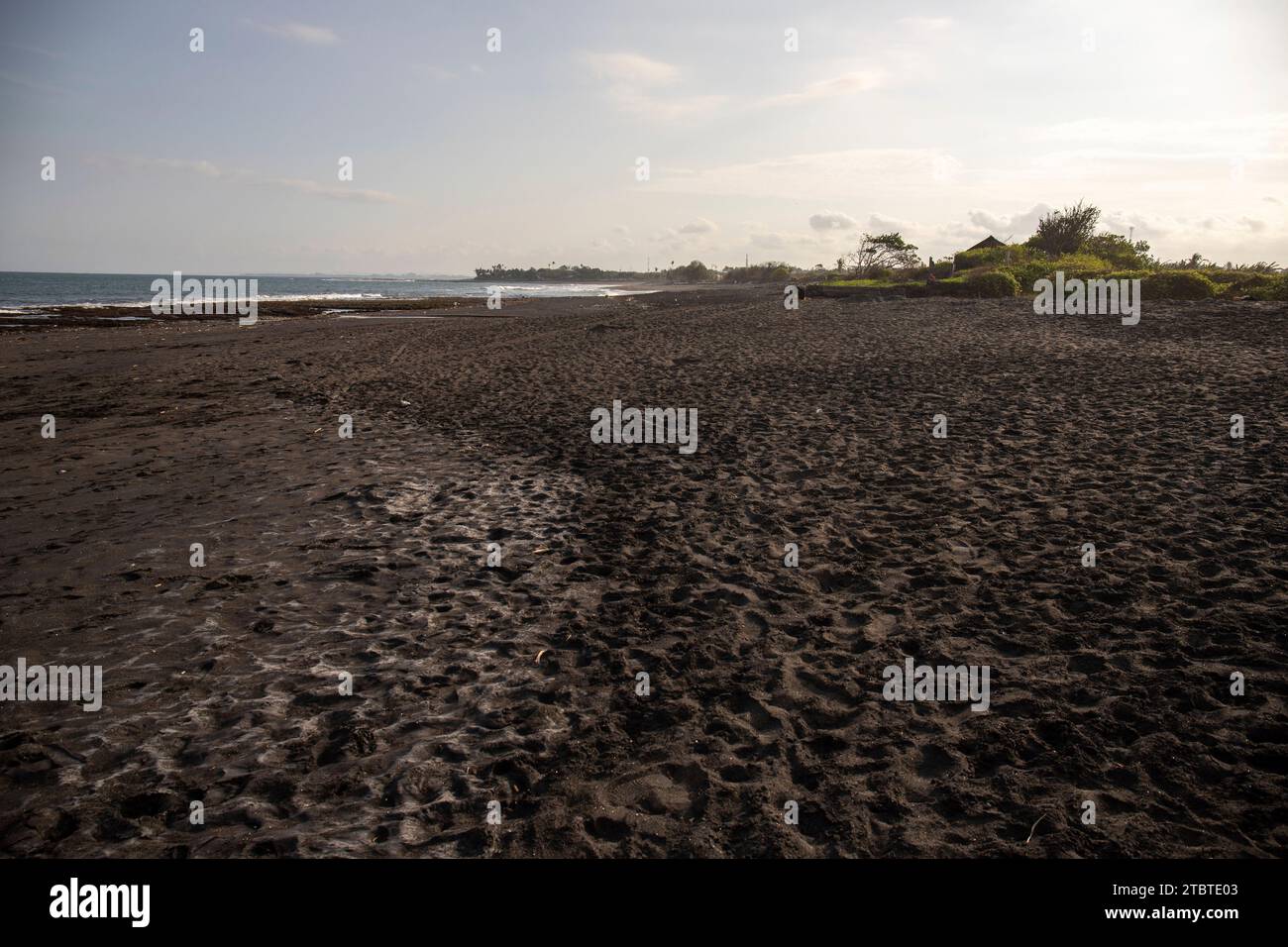 Una spiaggia di sabbia nera direttamente sul mare, splendida spiaggia con onde, spray e schiuma a Sanur, sull'isola di Bali, Indonesia, in bianco e nero Foto Stock