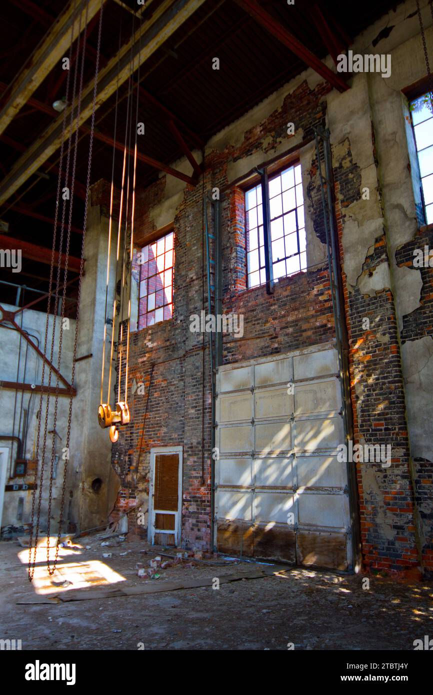 Interno del magazzino industriale abbandonato con muratura deteriorata e paranco a catena manuale Foto Stock