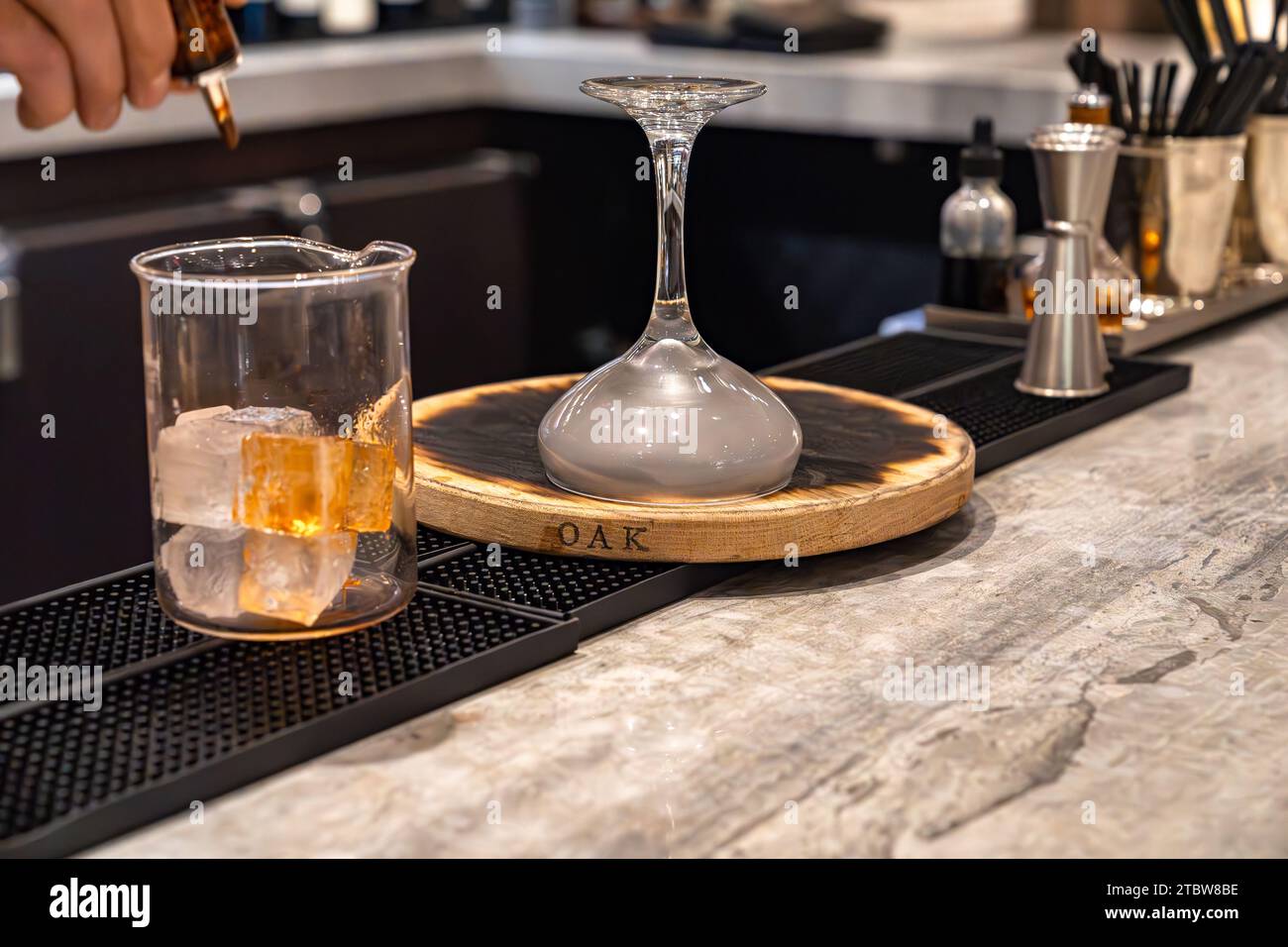 Il barista prepara un cocktail con whisky affumicato con bicchiere di vetro e un bicchiere da cocktail pieno di fumo Foto Stock