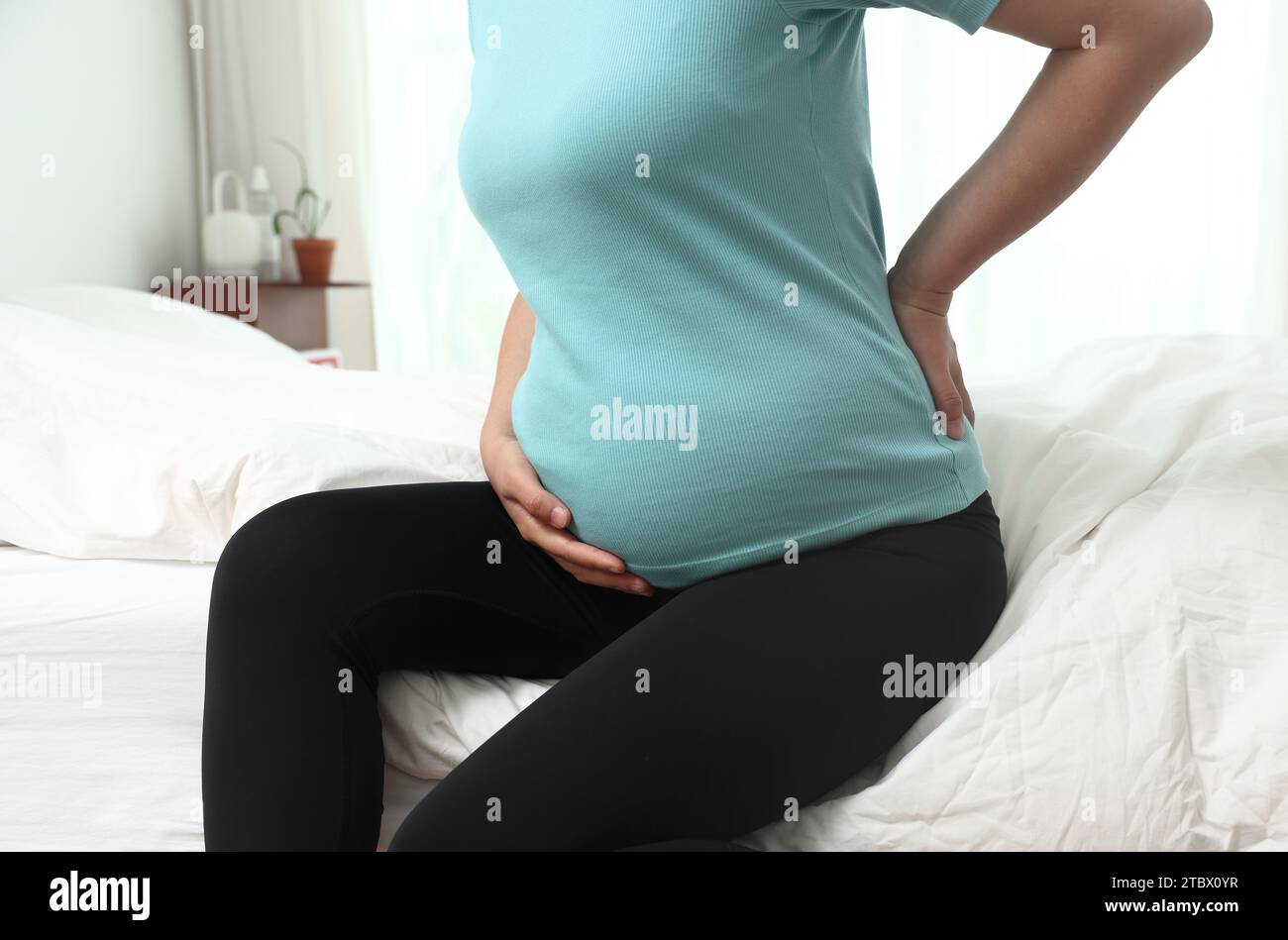 Una donna incinta è seduta sul letto toccando la schiena dolorosa Foto Stock