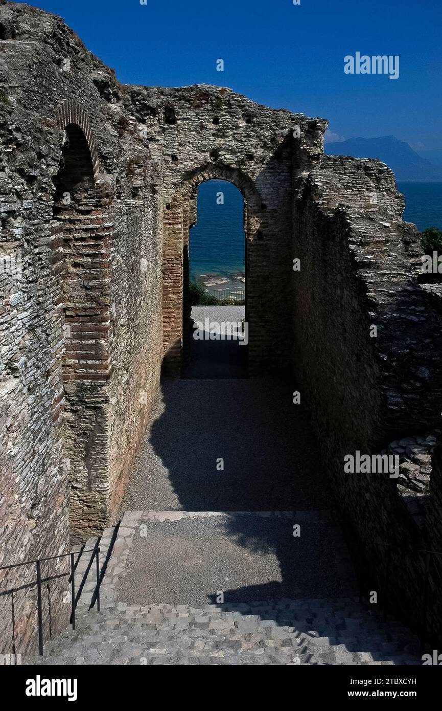 Veduta del Lago di Garda in Lombardia, Italia, attraverso stretti archi di una villa romana in rovina o di una casa di campagna, le Grotte di Catullo, a Sirmione in Lombardia, Italia. La villa fu costruita tra la fine del i secolo a.C. e il II secolo d.C. sulla penisola di Sirmio, promontorio all'estremità meridionale del Lago di Garda Foto Stock