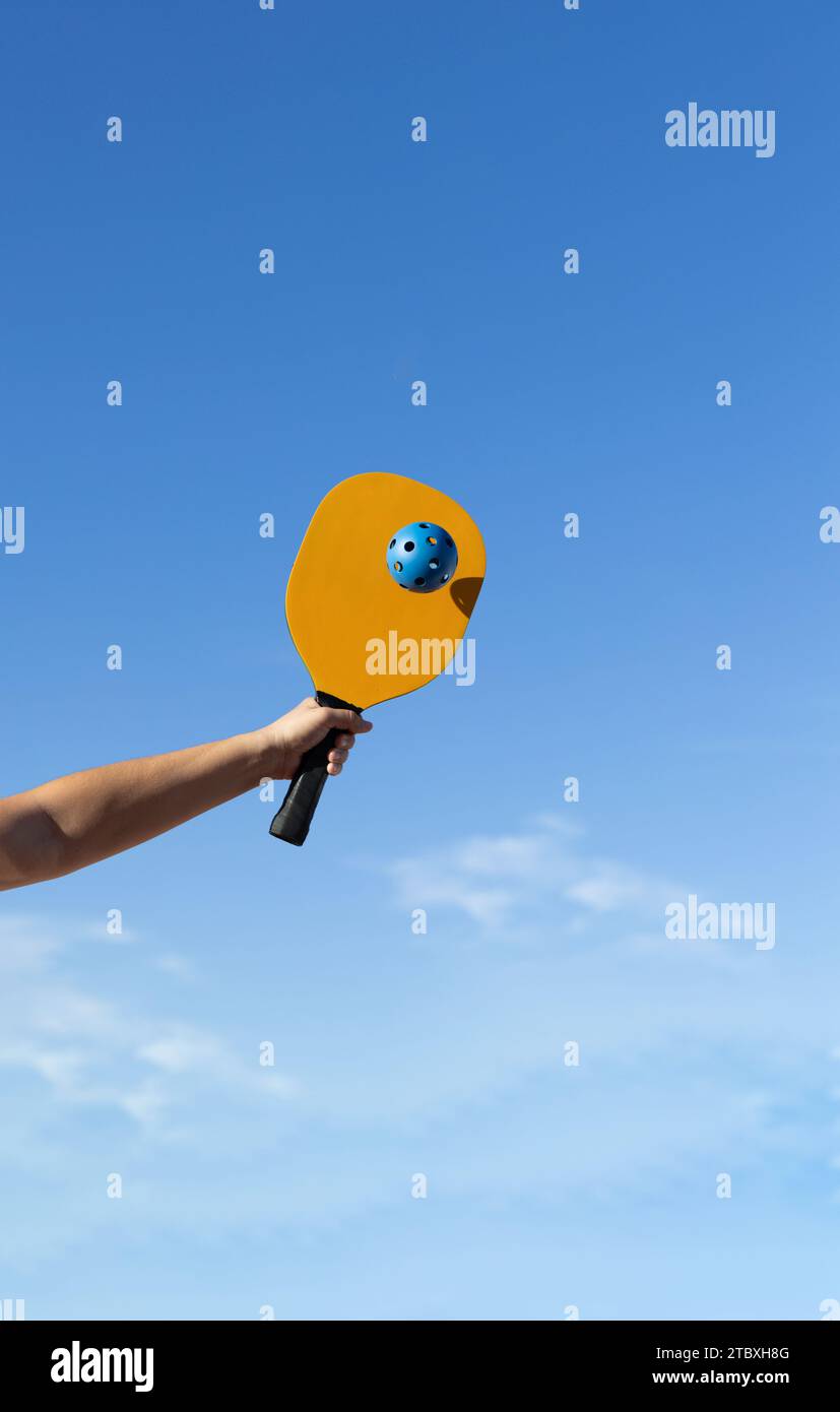 Armato con la pagaia gialla di Pickleball e colpire una palla blu in una partita Foto Stock