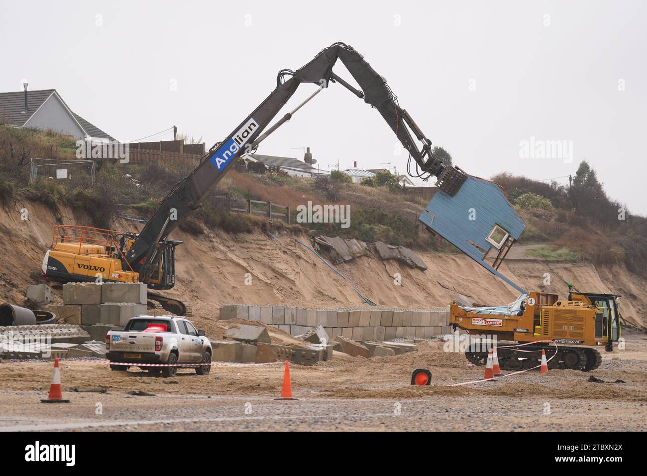 Gli operai demolitori abbattono la seconda di cinque case sulla scogliera nel villaggio di Hemsby, che è stata colpita dall'erosione costiera. L'alta marea e i forti venti hanno causato il crollo di un tratto di strada privata ad Hemsby, nel Norfolk, il mese scorso. Data immagine: Sabato 9 dicembre 2023. Foto Stock