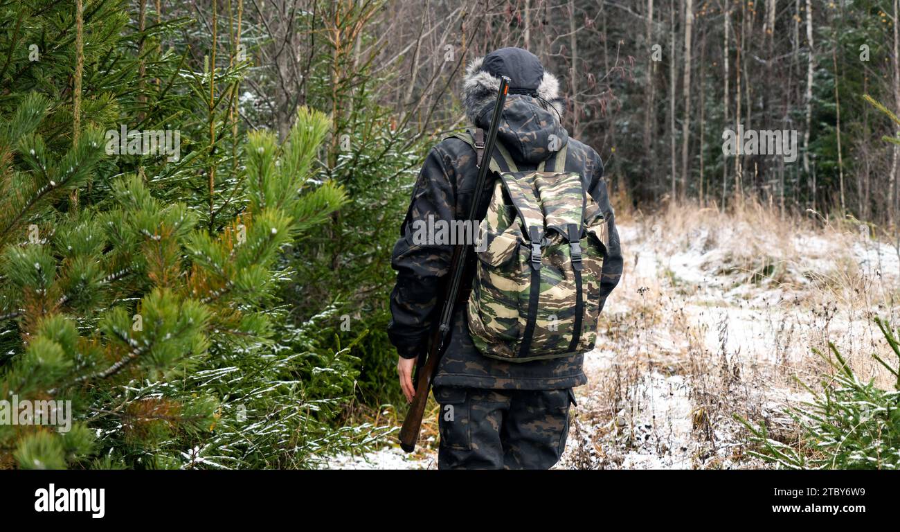 Cacciatore maschio mimetico e con zaino, armato di fucile, cammina attraverso la foresta invernale innevata. Foto Stock