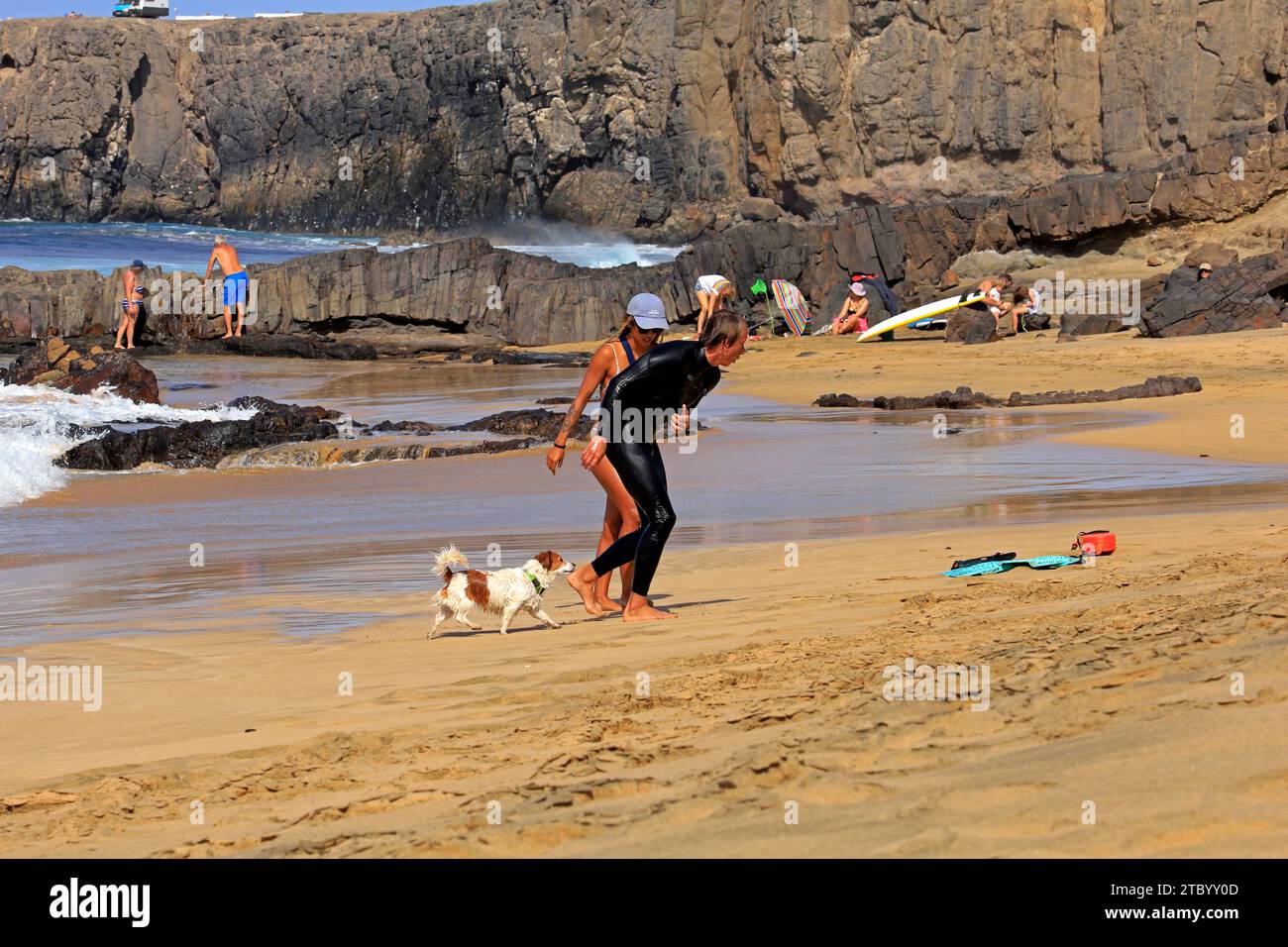 Donna che aiuta un surfista ferito, con un cane da compagnia preoccupato, El Cotillo, Fuerteventura, Isole Canarie, Spagna. Fatto nel novembre 2023 Foto Stock