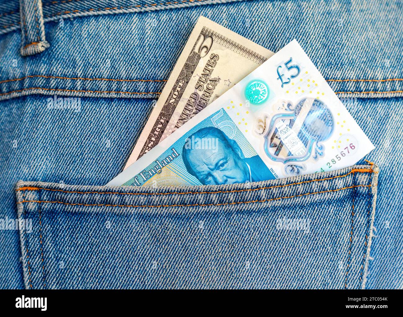 Banconota britannica da cinque sterline e cinque dollari americani che escono dalla tasca posteriore dei jeans per viaggiare e fare shopping Foto Stock