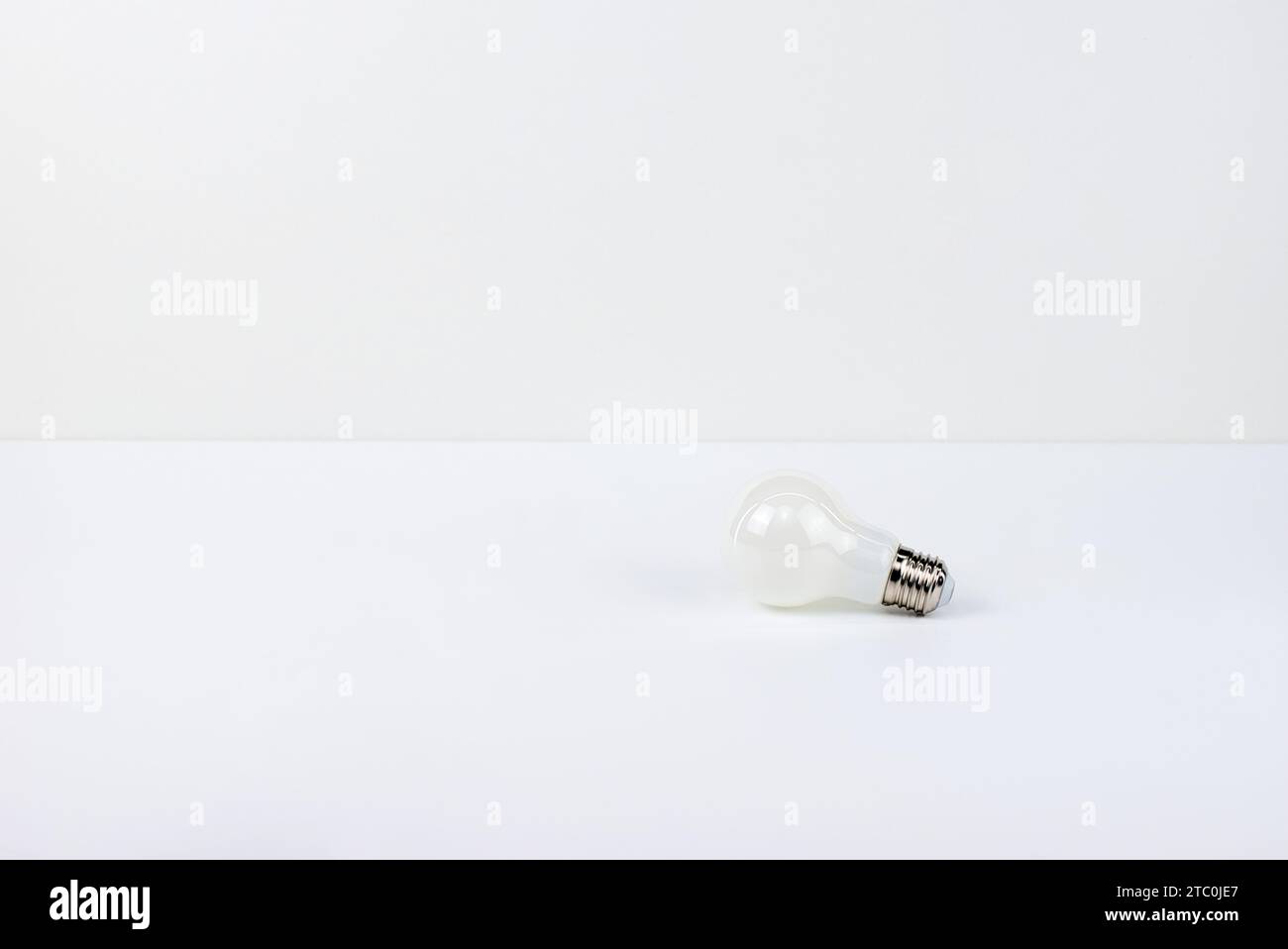 Lampadina singola posizionata su una superficie bianca su uno sfondo luminoso. Composizione pulita e minimalista, perfetta per trasportare semplicità e. Foto Stock