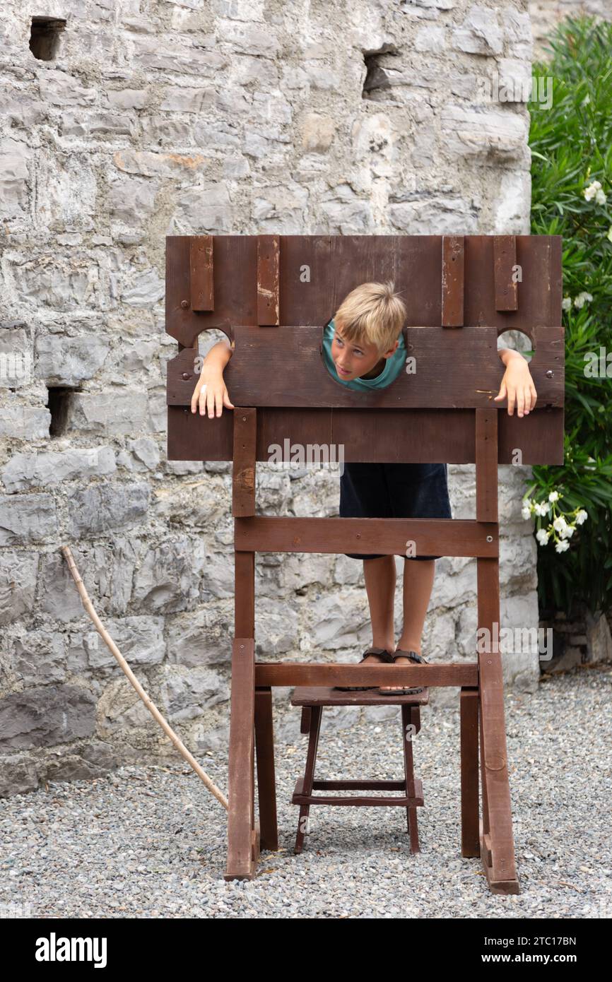 Un bambino finge di essere prigioniero in una replica della gogna tra le rovine del castello medievale di Vezio a Perledo, Lombardia, Italia. Foto Stock