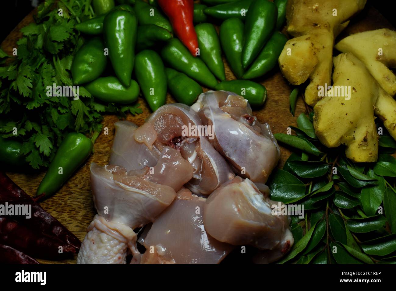 Aglio fresco, cipolla, freddo verde, pollo crudo, zenzero, foglie di coriandolo e foglie di curry su vassoio di legno con acqua cosparsa su quelle verdure. Foto Stock