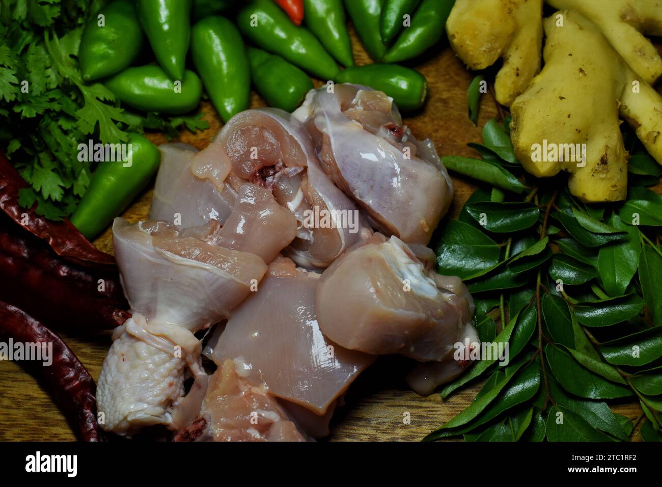 Aglio fresco, cipolla, freddo verde, pollo crudo, zenzero, foglie di coriandolo e foglie di curry su vassoio di legno con acqua cosparsa su quelle verdure. Foto Stock