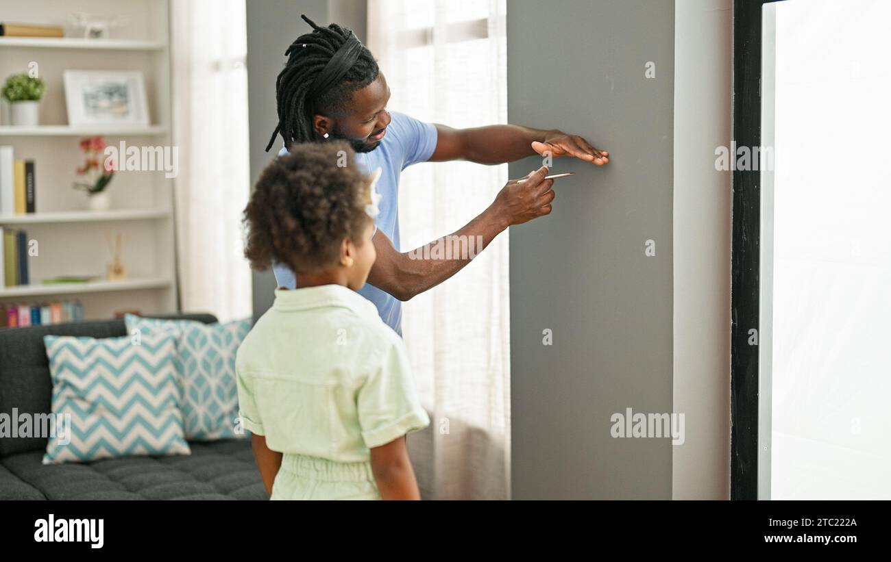Padre e figlia afro-americani sorridenti sicuri di misurare l'altezza sul muro a casa Foto Stock