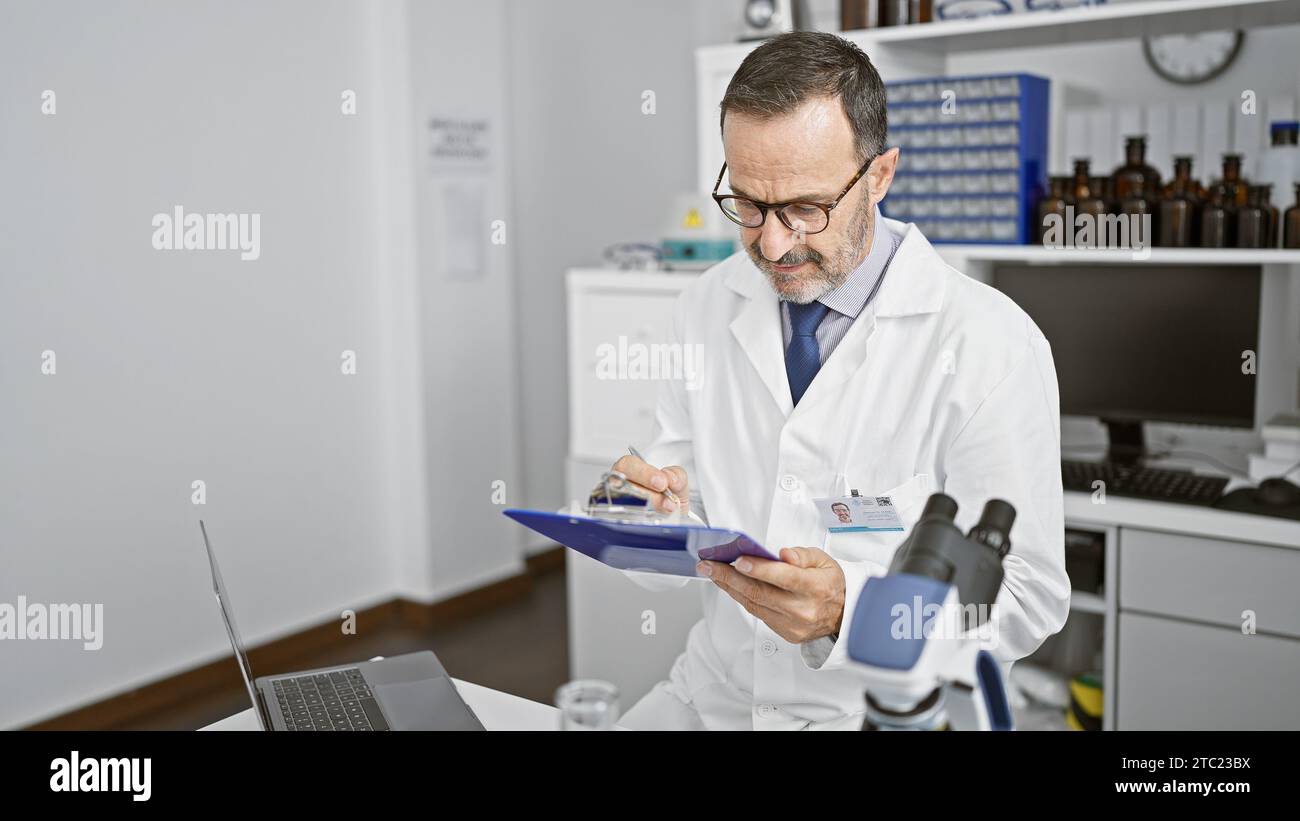 Un uomo serio di mezza età, scienziato dei capelli grigi, che prende appunti intensamente negli appunti del suo laboratorio di lavoro. coscienziosamente immerso nella ricerca medica con un Foto Stock