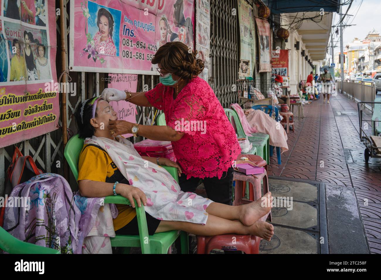 Bangkok, Thailandia. 8 dicembre 2023. Un membro del personale di un salone di bellezza di strada è visto mentre fa un face threading sul suo cliente su Charoen Krung Road. Chiamato "mang ming" in tailandese, il threading del viso è un antico metodo di depilazione originario della Cina, dell'India e del mondo arabo. Il metodo utilizza fili di cotone sottili come alternativa alla ceretta o alla pinzatura delle sopracciglia sottili e rimuove i peli superflui del viso. (Foto di Nathalie Jamois/SOPA Images/Sipa USA) credito: SIPA USA/Alamy Live News Foto Stock