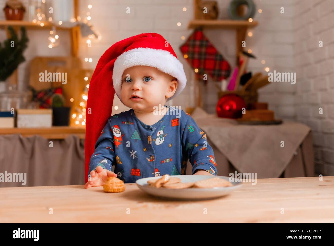 Un bambino carino in un cappello di Babbo Natale in cucina che mangia biscotti il giorno di Natale. Foto di alta qualità Foto Stock