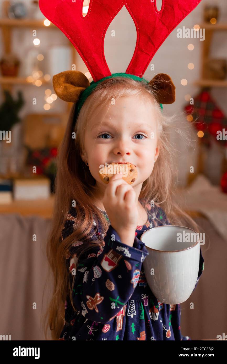 La bambina carina mangia biscotti al cacao in cucina a Natale a casa. Foto di alta qualità Foto Stock