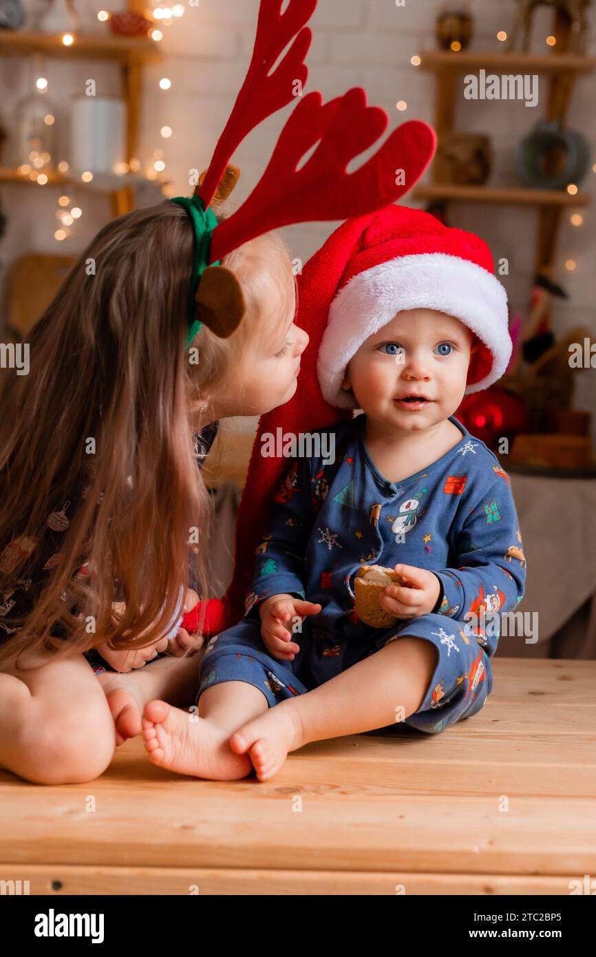 Due bambini, un ragazzo e una ragazza, mangiano biscotti in cucina il giorno di Natale. Foto di alta qualità Foto Stock